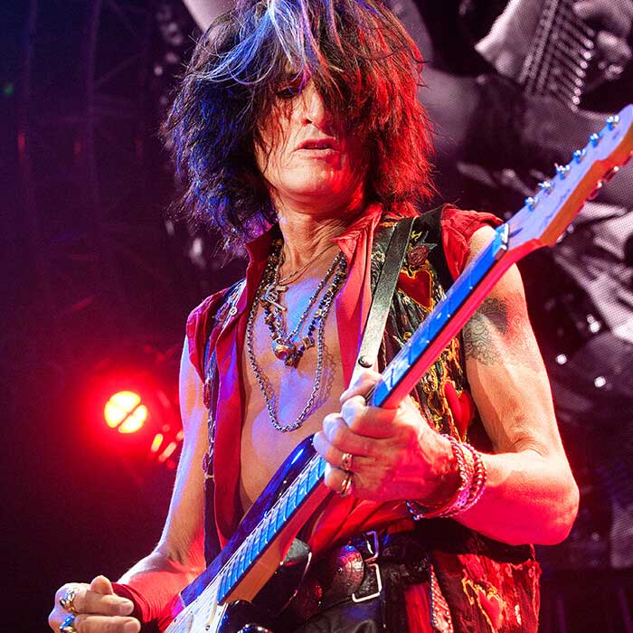 Joe Perry performing with Aerosmith while wearing a Red Monkey Slasher leather guitar strap.